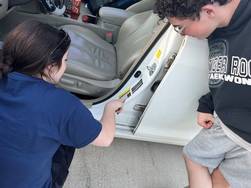 Beauregard FFA members Ava Barker (left) and Michael Pope (right) check the informational sticker on the door panel of a vehicle to find the recommended tire pressure. Photo courtesy of Jerad Dyess.