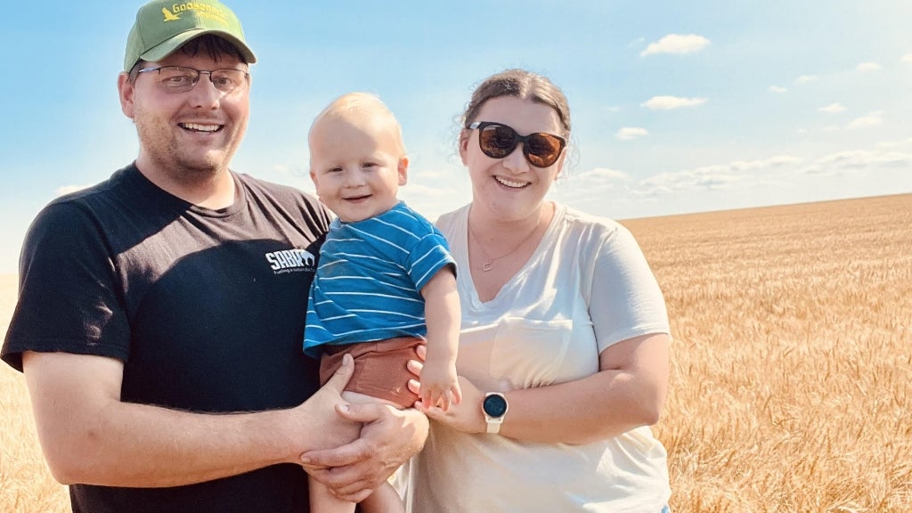 Josh Stutrud (left) smiles with his wife, Morgan (right), and son, Stelle (center), in a wheat field before harvest last fall. Photo courtesy of Josh Stutrud.