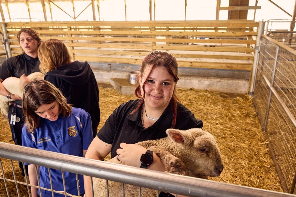 MHS student Harleigh Myers stops and smiles with one of the sheep being raised in her school’s Animal Center. Photo by Chris Simpson.