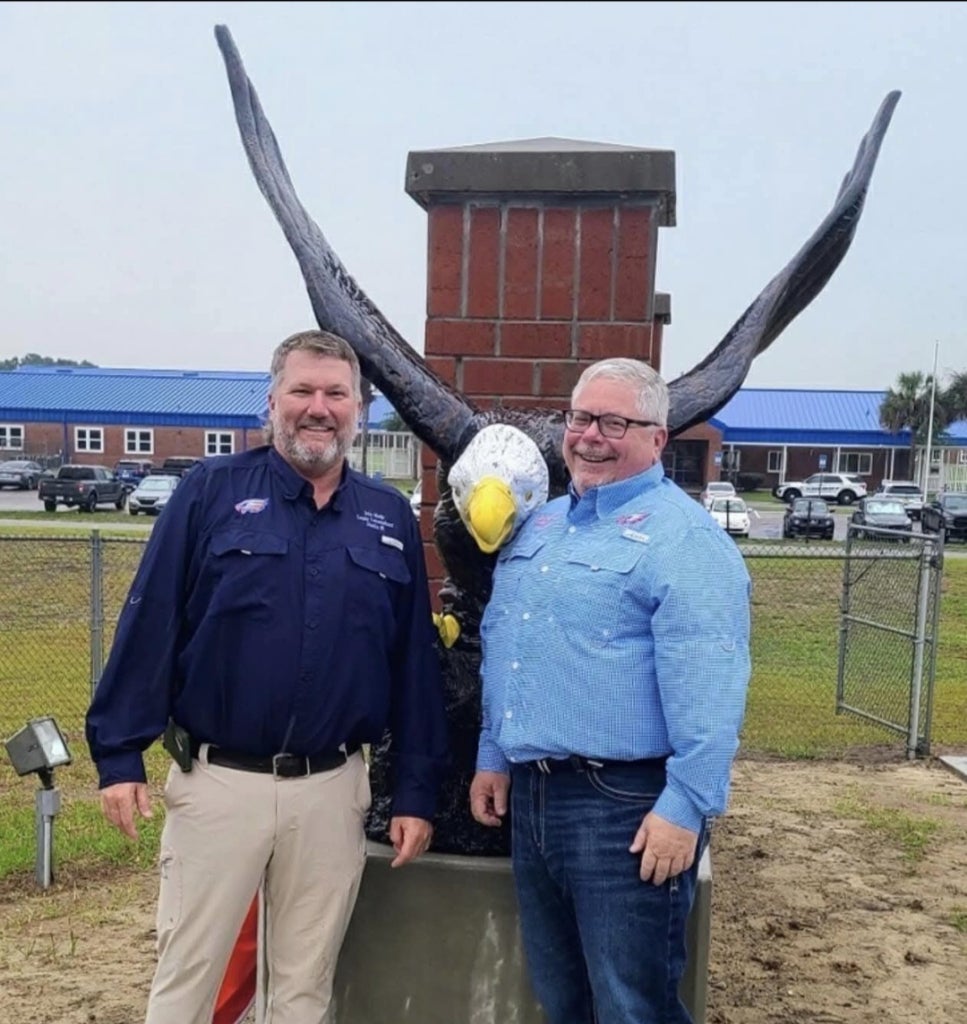 Cameron Asbell (right) stands next to John Meeks (left) in Front of an eagle statue they donated to Bronson Middle High School reflecting how they serve their community.