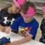 Shattuck Kindergarten student, Westin Burns, practicing giving shots at the vet science station with the help of Shattuck FFA Senior Avery Quisenberry while wearing his ear notched headband from an ear notching station.