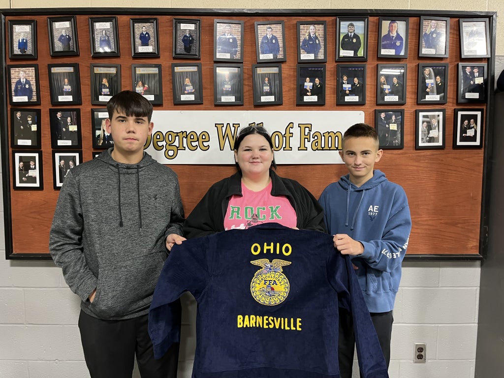 Three Barnesville FFA freshman – Caleb Bush, Chloe Gordon and Aiden Starr – stand in front of the Degree Hall of Fame and hold their new blue FFA jacket embroidered with “Ohio” and “Barnesville.”