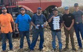 FFA members and local farms stand in front of a combine holding boxes of food.
