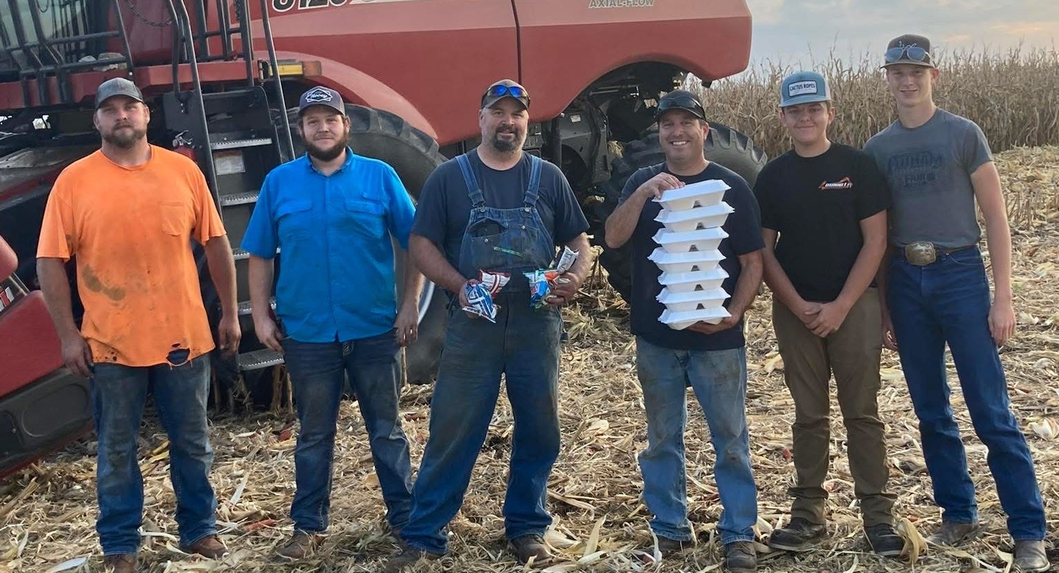 FFA members and local farms stand in front of a combine holding boxes of food.