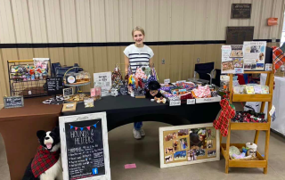 Ava sets up her products at an indoor booth.