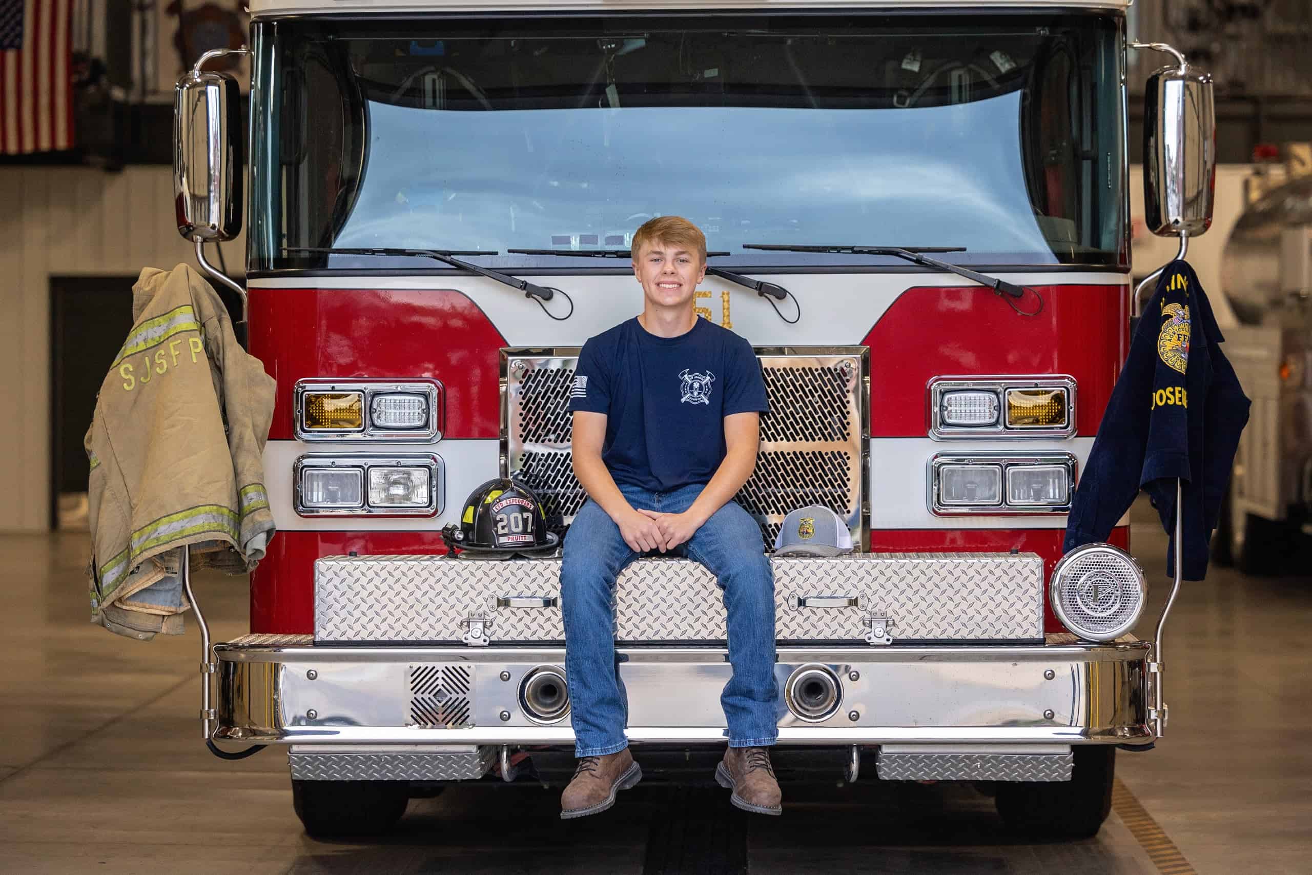 Pruitt sits on a SJSFPD fire truck with his firefighter jacket on one side, and his FFA jacket on the other.