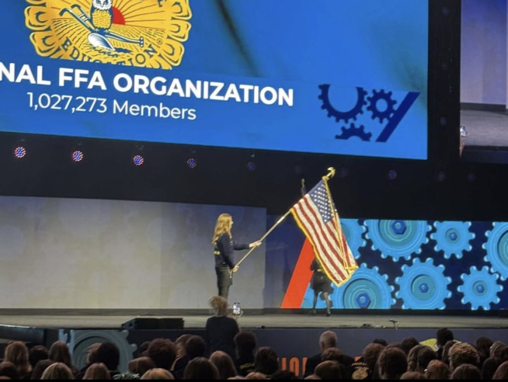 Julia Pierce holds the American flag on stage during the opening session at the 97th National FFA Convention & Expo.