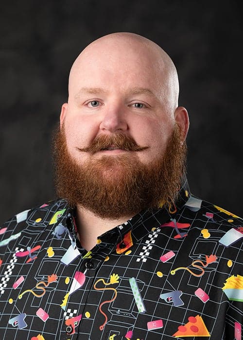 : ⁠Official professional headshot portrait of Dr. O.P. McCubbins smiling, wearing a dark patterned button-down shirt against a clean, neutral background.⁠
