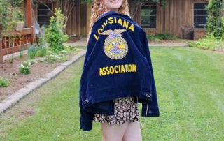 Young woman wearing Louisiana FFA jacket smiling outdoors in backyard.
