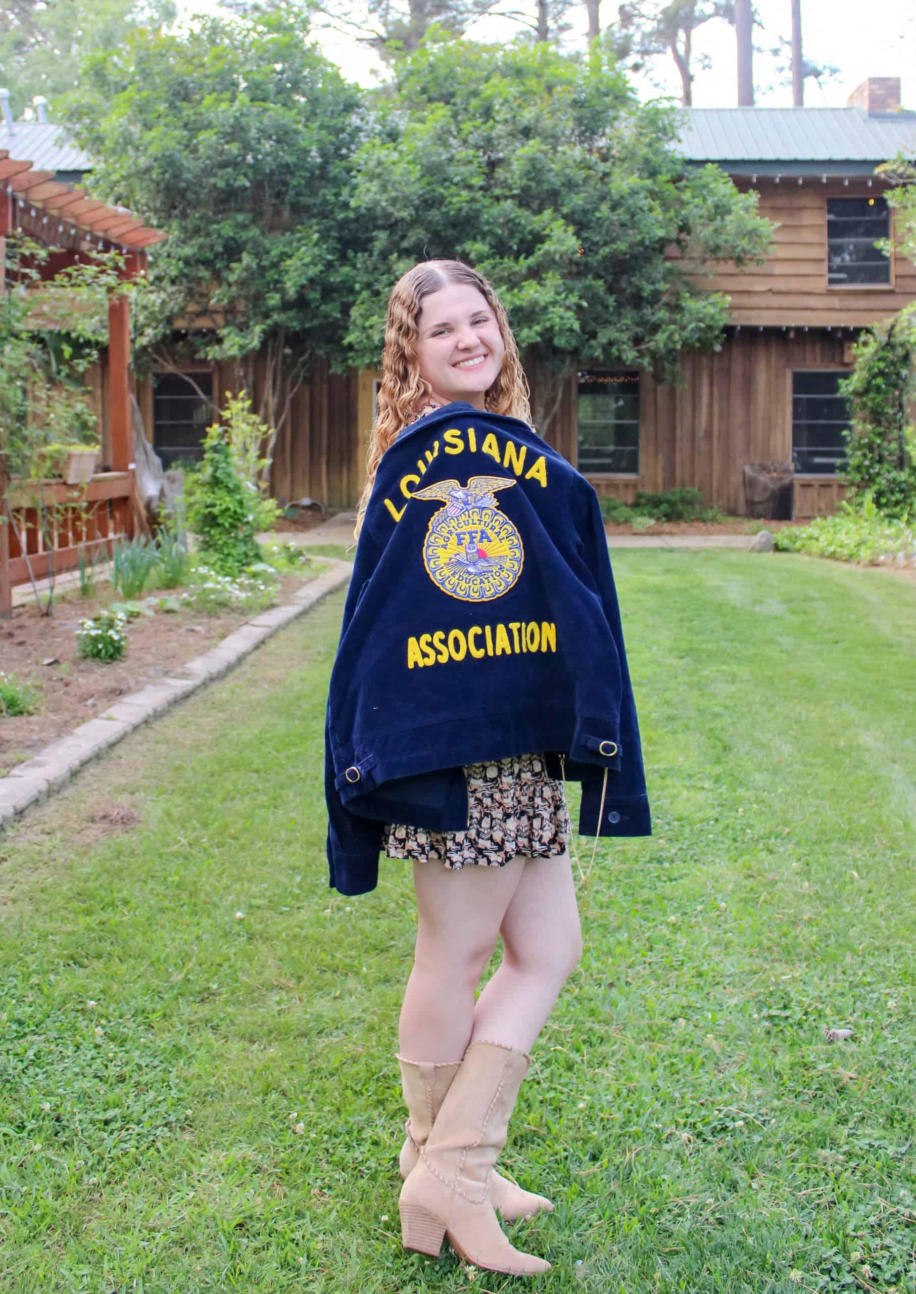 Young woman wearing Louisiana FFA jacket smiling outdoors in backyard.