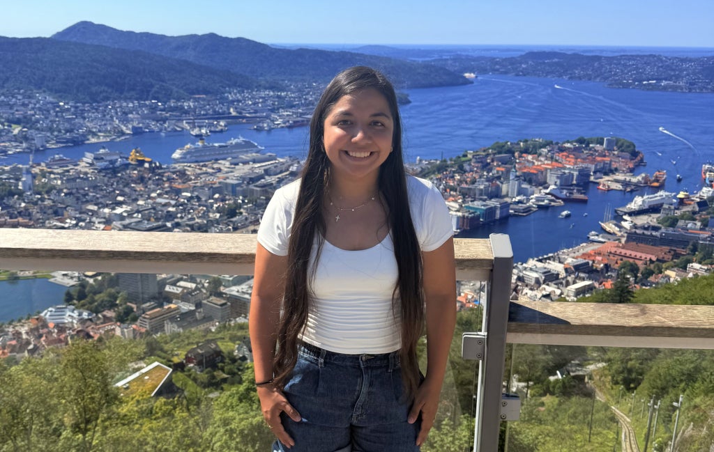 Hannah Gordon, an agriculture teacher at the North Carolina School for the Deaf, stands before a seaside town surrounded by mountains during an overseas experience made possible by the Lyle E. Orwig International Travel Grant for Agriculture Educators.