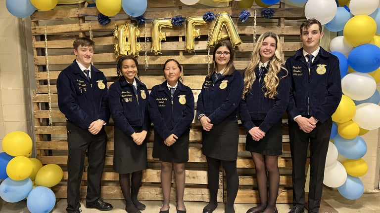 FFA members stand in official dress in front of a blue and gold balloon arch