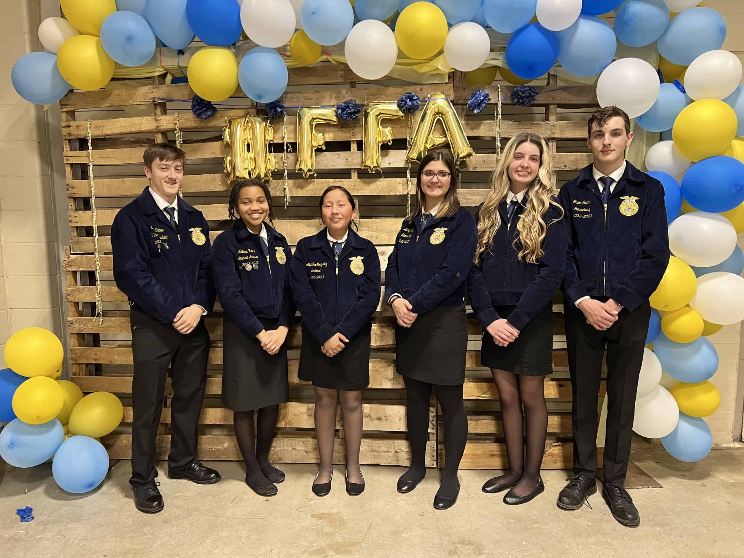 FFA members stand in official dress in front of a blue and gold balloon arch