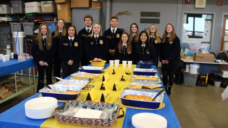 FFA members stand in front of a table with a buffet of food with blue and gold table cloth